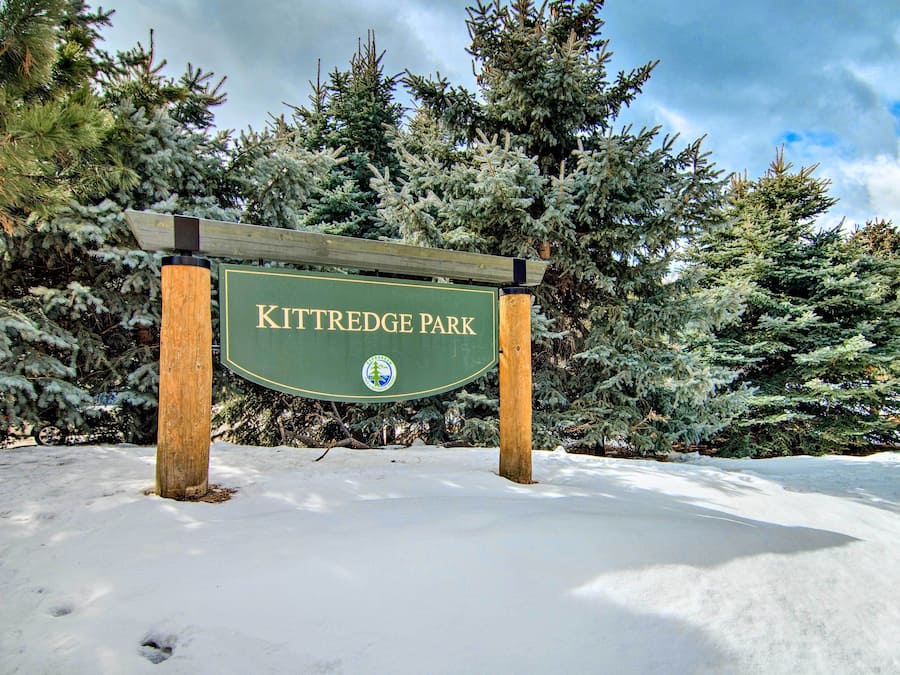 A sign for Kittredge Park surrounded by snow-covered trees.
