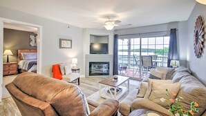 A modern living room with a fireplace, a ceiling fan, and a large window offering a view of the outdoors. - Screened Balcony w/ Views: Sleek Lake Ozark Gem! (Lake Ozark)