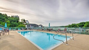 A rectangular pool with metal ladders, surrounded by lounge chairs and a fence, with buildings and trees in the background. - Screened Balcony w/ Views: Sleek Lake Ozark Gem! (Lake Ozark)