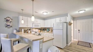 A modern kitchen with white cabinets, a central island with bar stools, a refrigerator, and a microwave. - Screened Balcony w/ Views: Sleek Lake Ozark Gem! (Lake Ozark)