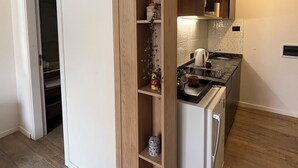 A compact kitchen with a built-in wooden cabinet, a white refrigerator, and a countertop with a kettle. - Trendy Loft in Güemes - Walk to Art, Bars & Antiques (Unquillo asociacion civil corral de barrancas)