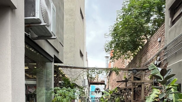 A narrow alleyway with potted plants on both sides, leading to a building with a blue door and a sign. - Trendy Loft in Güemes - Walk to Art, Bars & Antiques (Unquillo asociacion civil corral de barrancas)