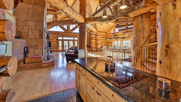 A spacious log cabin interior with a large kitchen area featuring a granite countertop and a built-in stove.