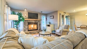 Una sala de estar acogedora con chimenea de piedra, un sofá beige grande, una mesita de centro redonda y un sillón cómodo.