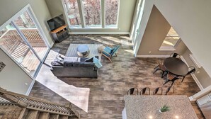 A spacious living area with a large window, a fireplace, a dining table, and a staircase.