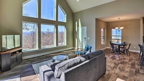 A spacious living room with large windows, a fireplace, a dining area, and a modern kitchen.
