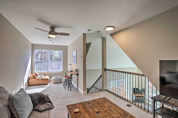 Ein geräumiges Wohnzimmer mit Deckenventilator, einem Holztisch, einer Couch und einer Treppe, die zu einem Balkon führt.