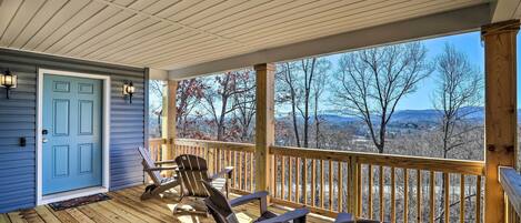 A covered porch with wooden railings, a blue door, and Adirondack chairs.