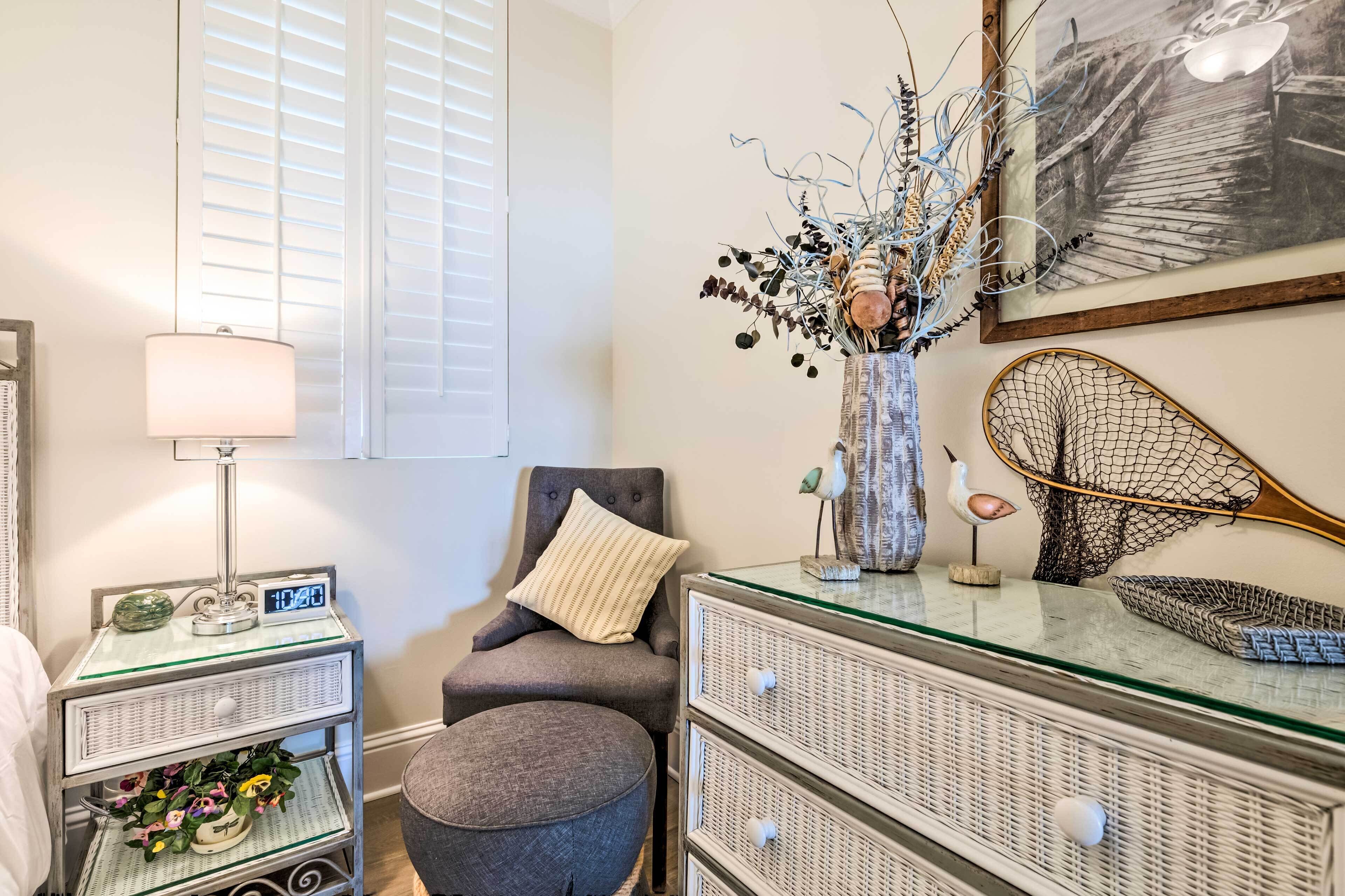 A neatly arranged bedroom with a bedside table, lamp, chair, and a dresser with drawers.