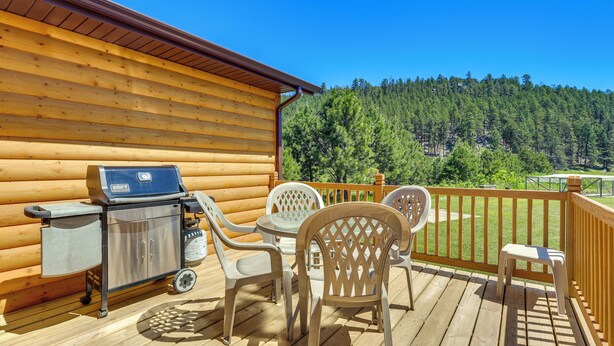 A wooden deck with a grill, chairs, and a table. - Rapid City Cabin w/ Hiking & ATV Trail Access (Rapid City)