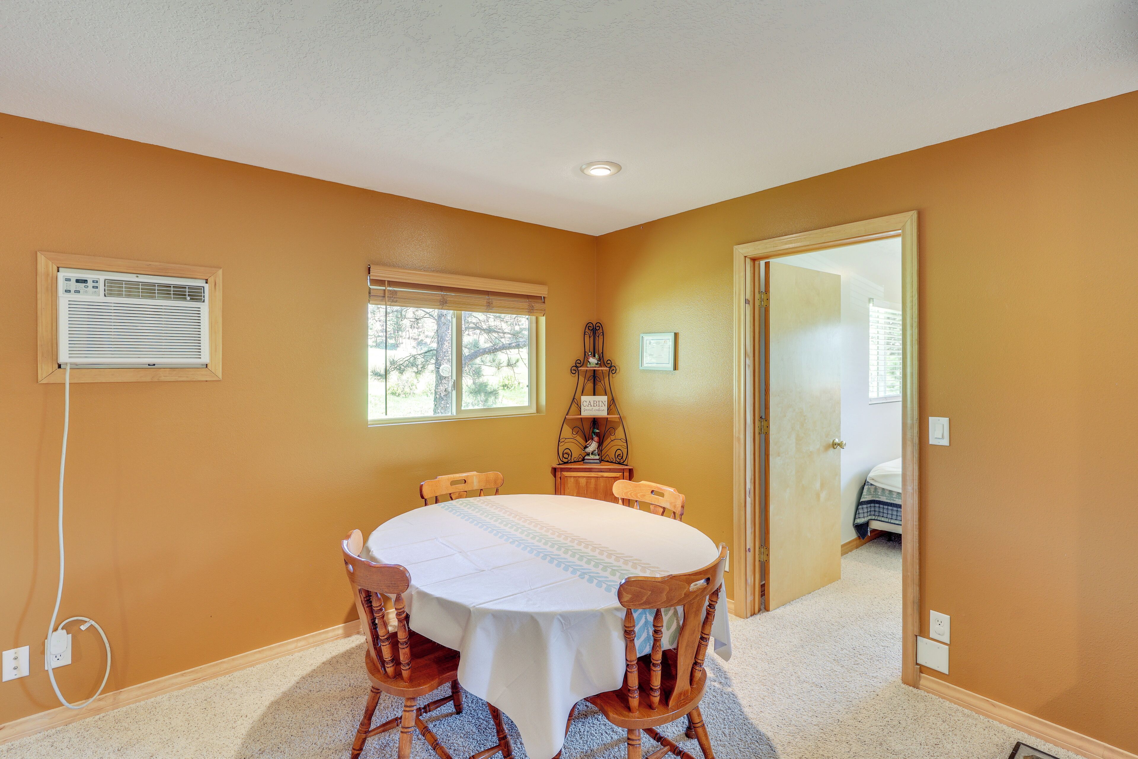 A dining area with a round table, chairs, a window, and an air conditioning unit.