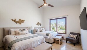 Een slaapkamer met twee bedden, een plafondventilator, een raam met uitzicht en decoratieve muurkunst.