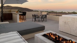 Eine Dachterrasse mit Feuerstelle, Sitzgelegenheiten im Freien und Blick auf die Landschaft.