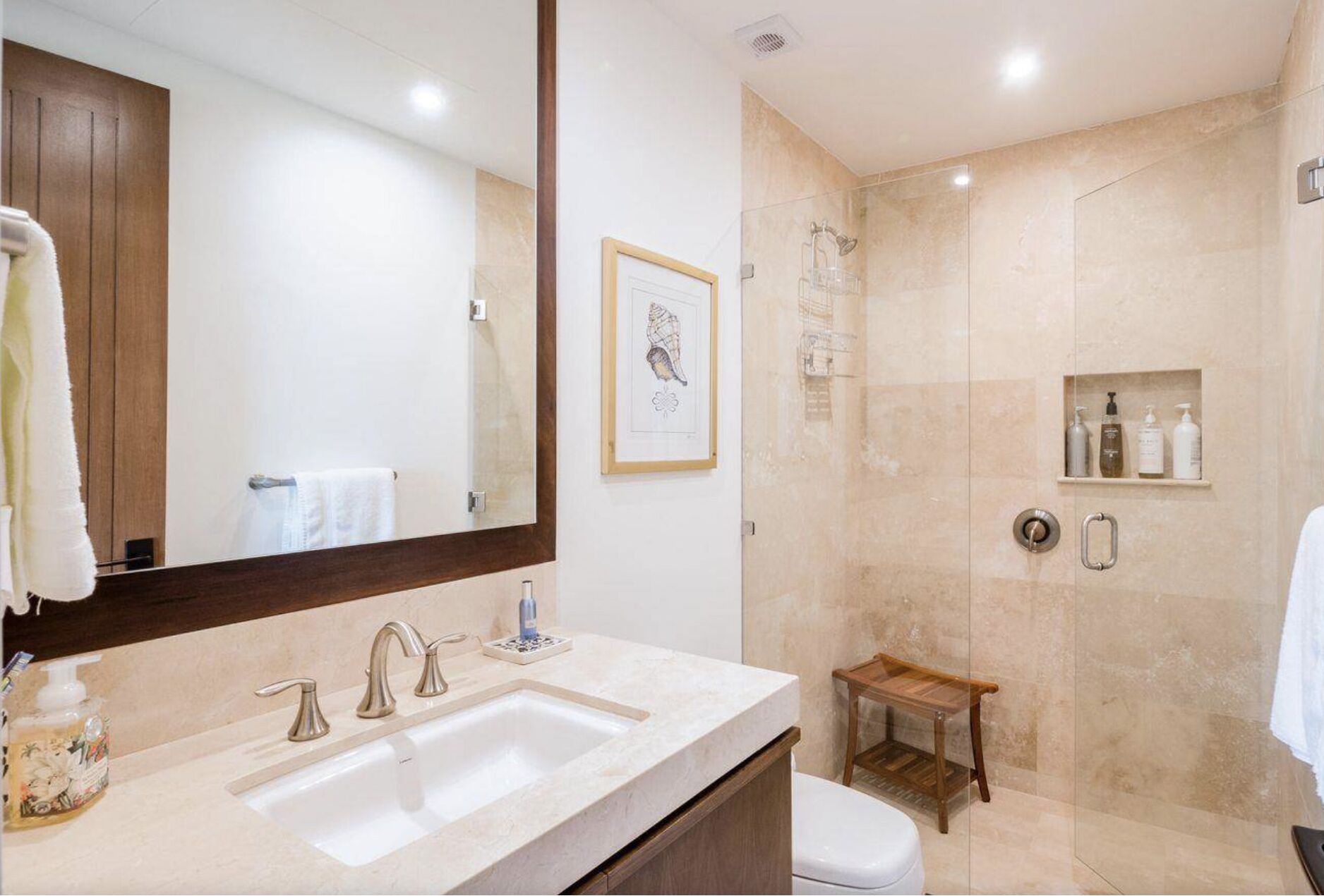Un baño moderno con un espejo grande, dos lavamanos, una ducha y un pequeño taburete de madera.