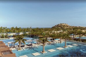 Zwembad van een resort met palmbomen, ligbedden en uitzicht op de oceaan.