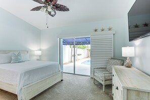 Una camera da letto con un letto, una cassettiera, un comodino, una ventola a soffitto e vista su una piscina attraverso una porta scorrevole in vetro.