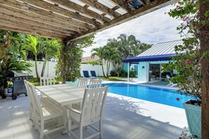 Una veranda coperta con piscina, mobili bianchi e barbecue.