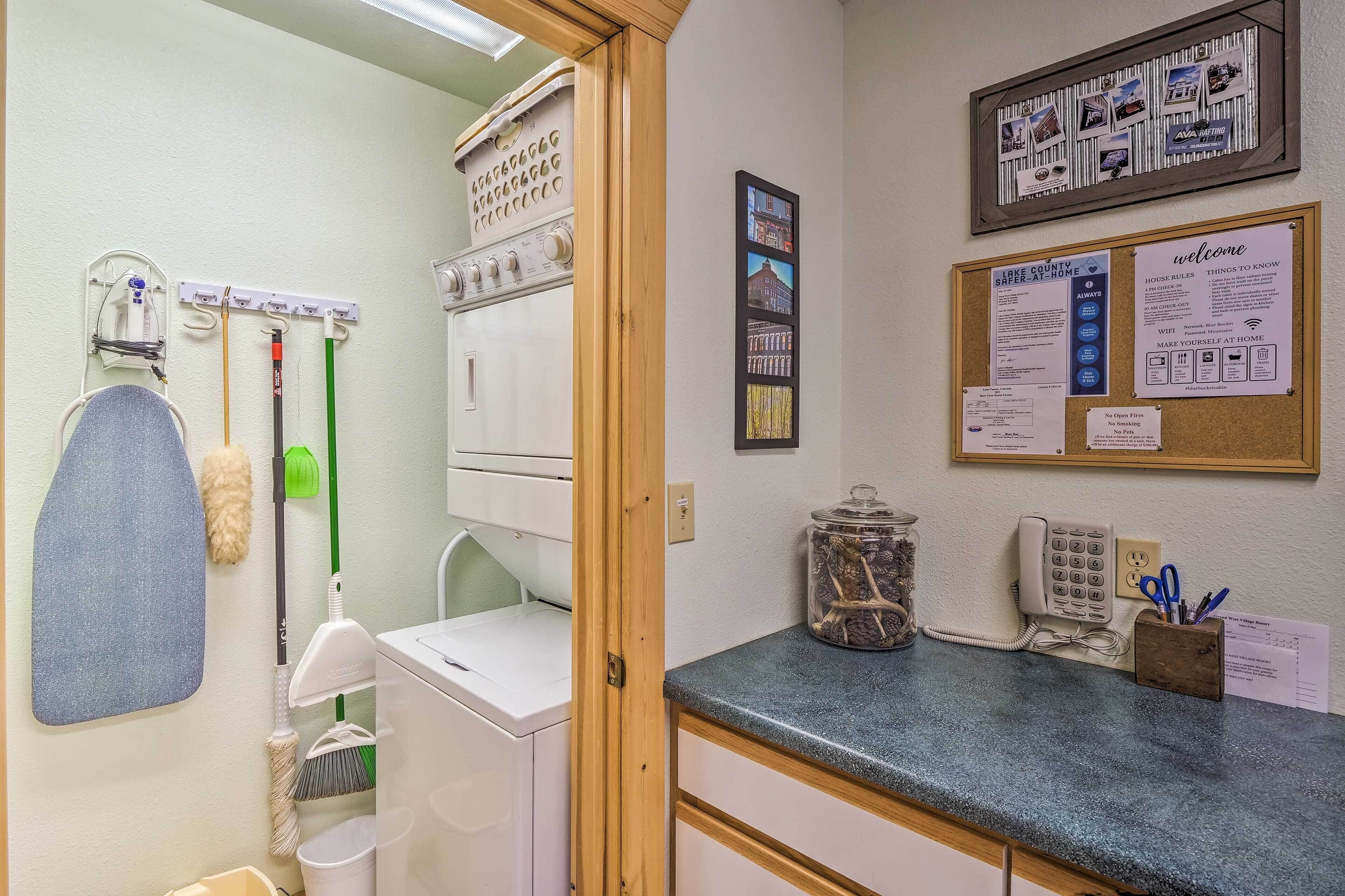 A laundry area with a washing machine, drying rack, and various cleaning tools. There is a bulletin board with notices and a welcome sign.