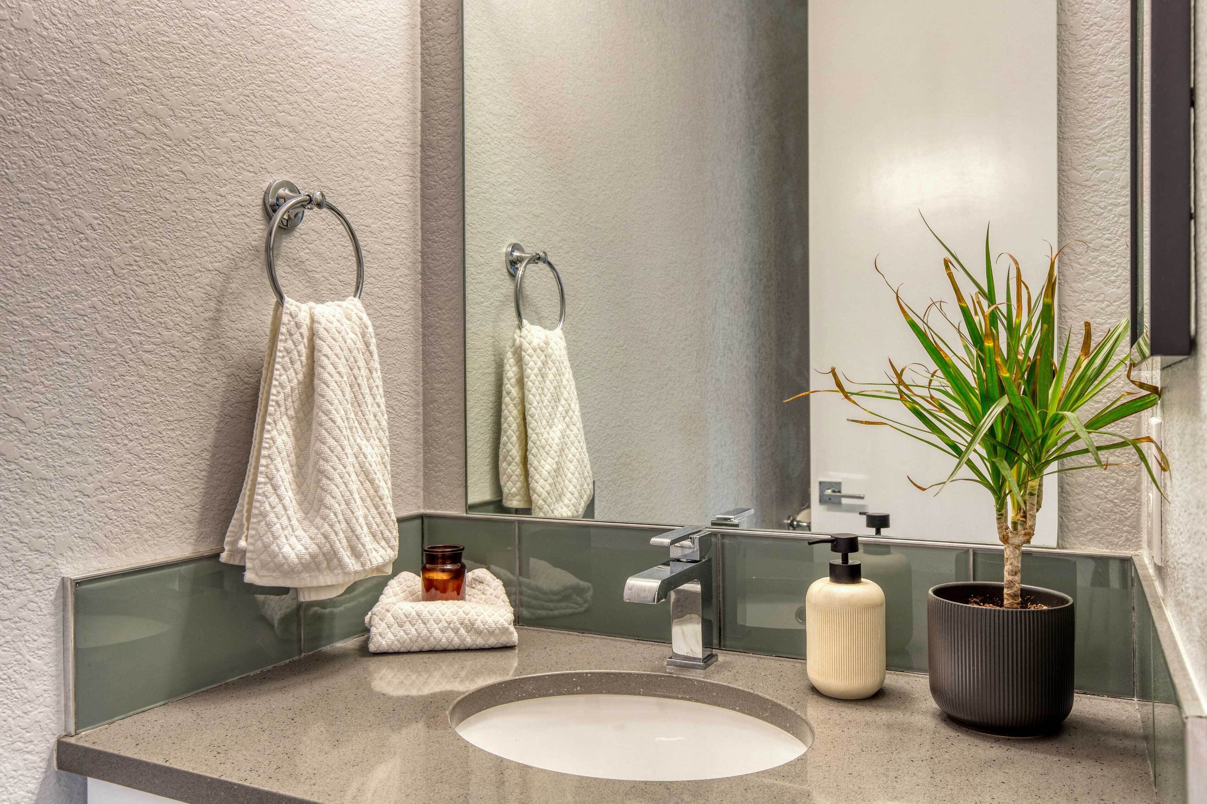 A bathroom with a round sink, a large mirror, two towels, a potted plant, and a soap dispenser.