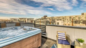 Tagterrasse med jacuzzi, en fletstol med pude og udsigt over bybilledet.