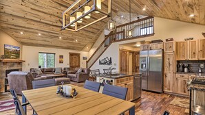 A spacious living area with a wooden dining table, a kitchen with wooden cabinets, and a staircase leading to an upper level. - Rocky Mountain Alma Cabin With Deck & Hot Tub! (Alma)