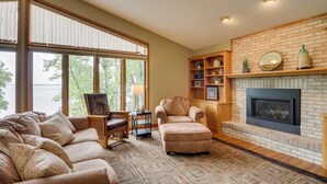 A cozy living room with a fireplace, large windows, and a view of the outdoors. - Sandy Beach Family Getaway w/ Fire Pit & Deck! (Alexandria)