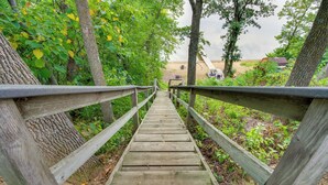 A wooden boardwalk leading to a beach area with trees and a sandy path. - Sandy Beach Family Getaway w/ Fire Pit & Deck! (Alexandria)