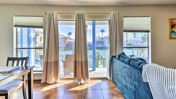 A room with a dining table, a sofa, and a view of a water body and buildings. - Padre Island Retreat on Canal - 2 Mi to Beach! (Corpus Christi)
