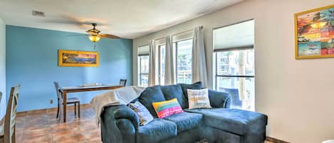 A living room with a dark blue sectional sofa, a dining table with chairs, and a ceiling fan.