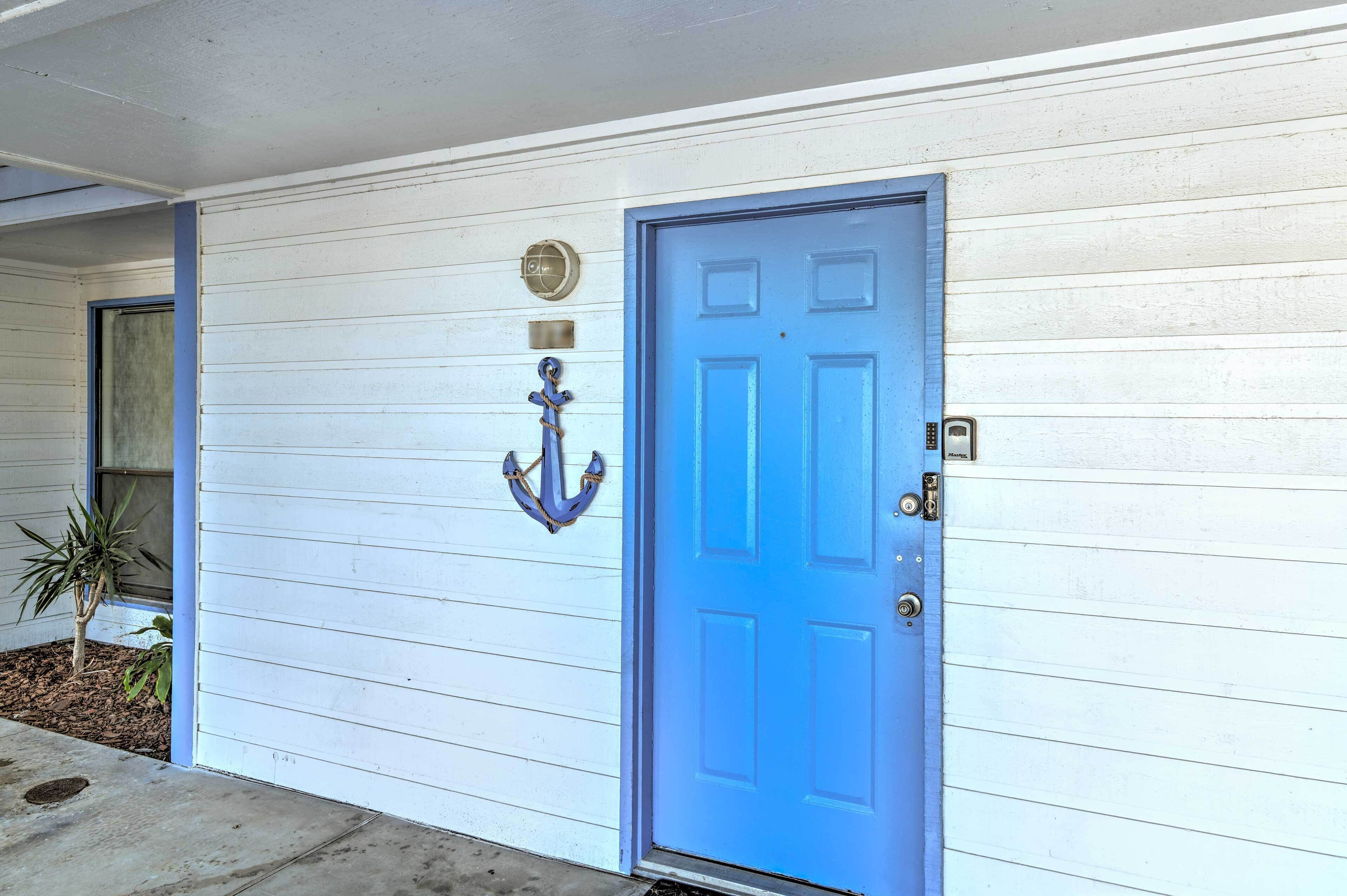 A white building with a blue door, a small plant, and a metal anchor decoration.
