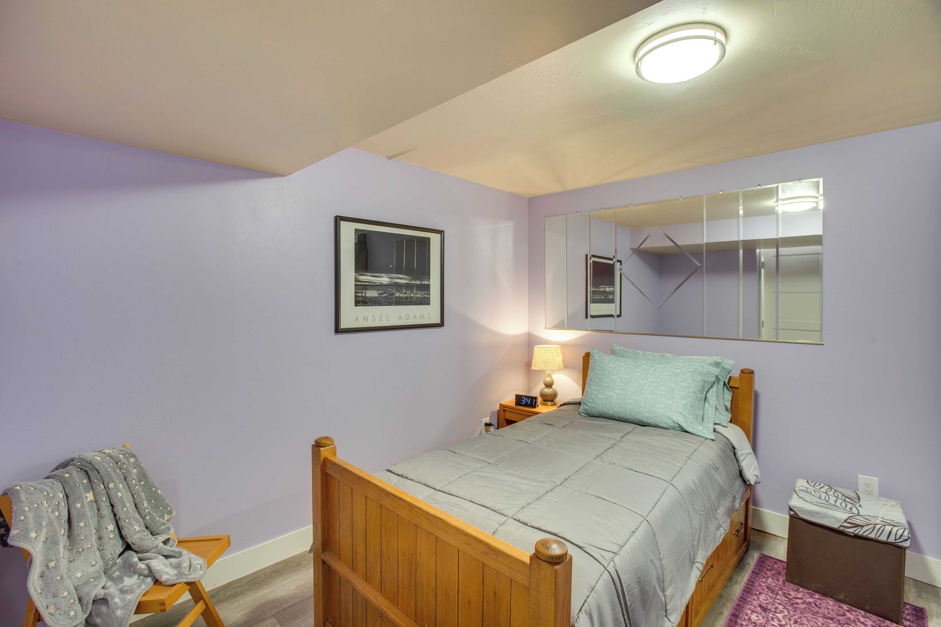 Een slaapkamer met een houten bed, een nachtkastje met een lamp, een spiegel en een lijst met een afbeelding aan de muur.