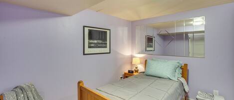 A bedroom with a wooden bed, a nightstand with a lamp, a mirror, and a framed picture on the wall.