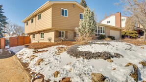 A two-story house with a sloped roof, a front porch, and a snow-covered yard with rocks and shrubs. - 9 Mi to Dtwn: Quiet South Denver Apartment (Lakewood)