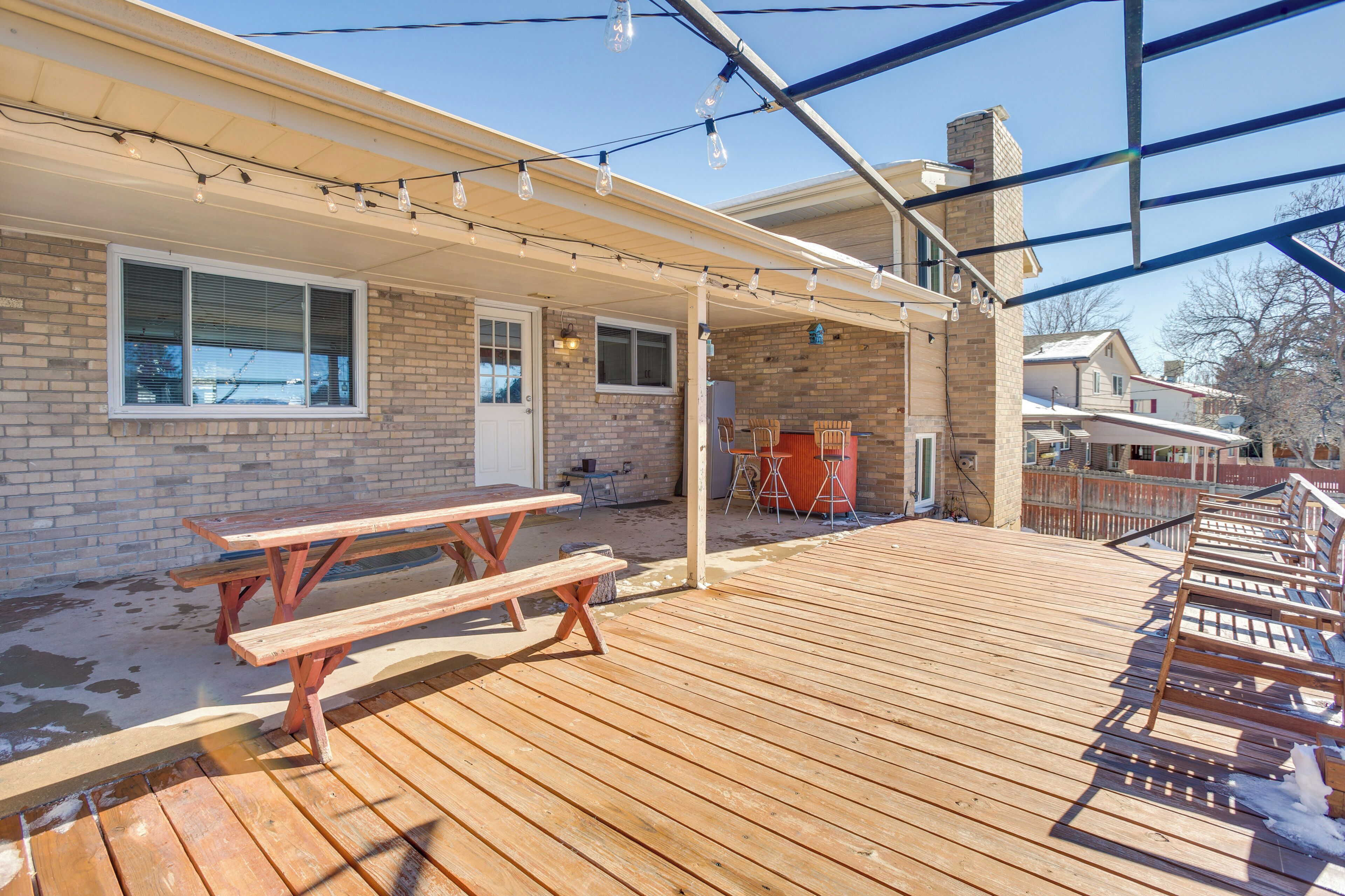 A wooden deck with picnic tables and benches, a covered patio area, and string lights.