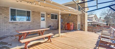 A wooden deck with picnic tables and benches, a covered patio area, and string lights.