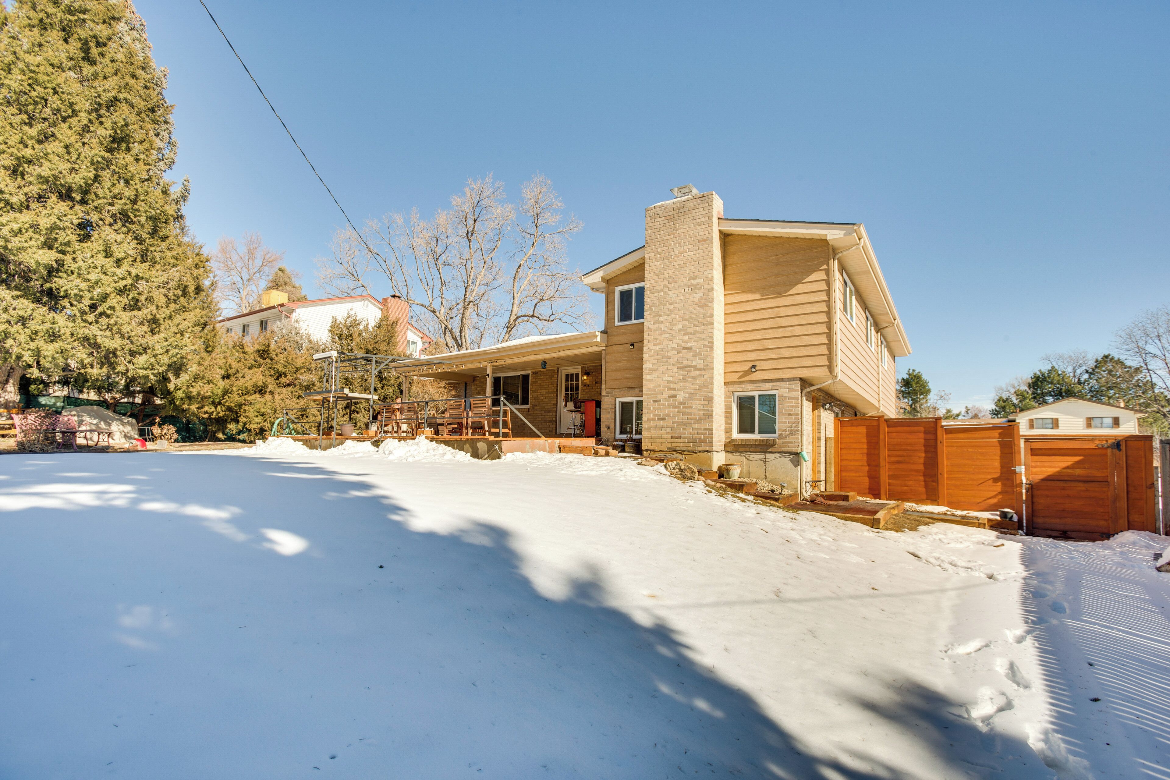 A two-story house with a brick chimney, a wooden deck, and a snow-covered yard.