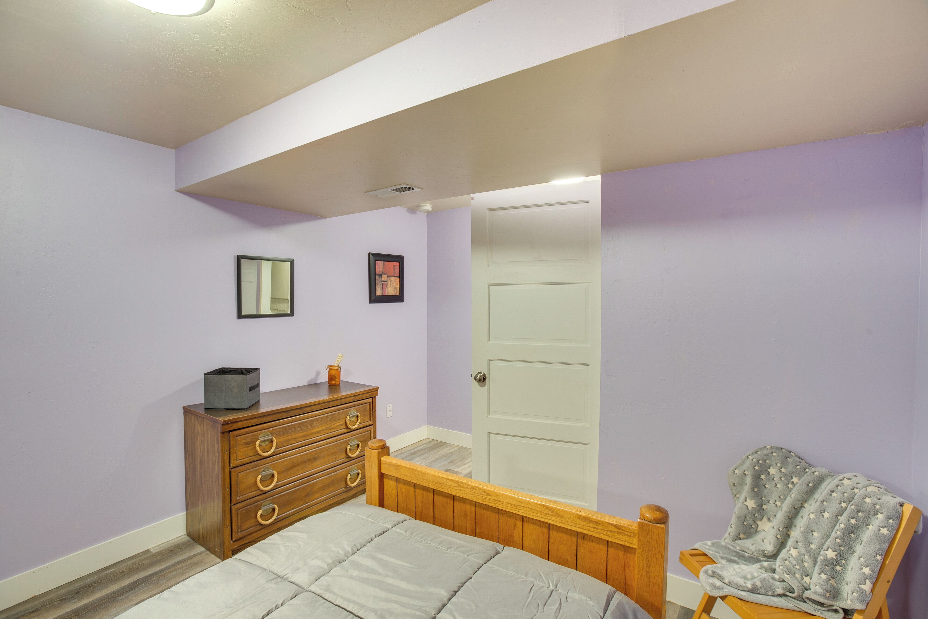 A bedroom with a bed, dresser, chair, and door.