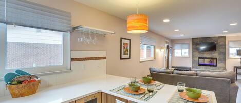 A modern kitchen with a dining area, featuring a built-in oven, a stone fireplace, and a large window with blinds.