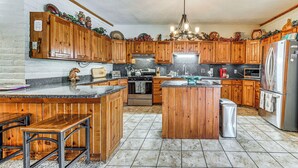 A kitchen with wooden cabinets, a central island, stainless steel appliances, and a chandelier. - Spacious Alto House on 8 Private Acres w/ Hot Tub! (Alto)