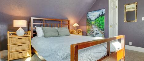A bedroom with a wooden bed, two bedside tables with lamps, a wall-mounted painting, and a door.