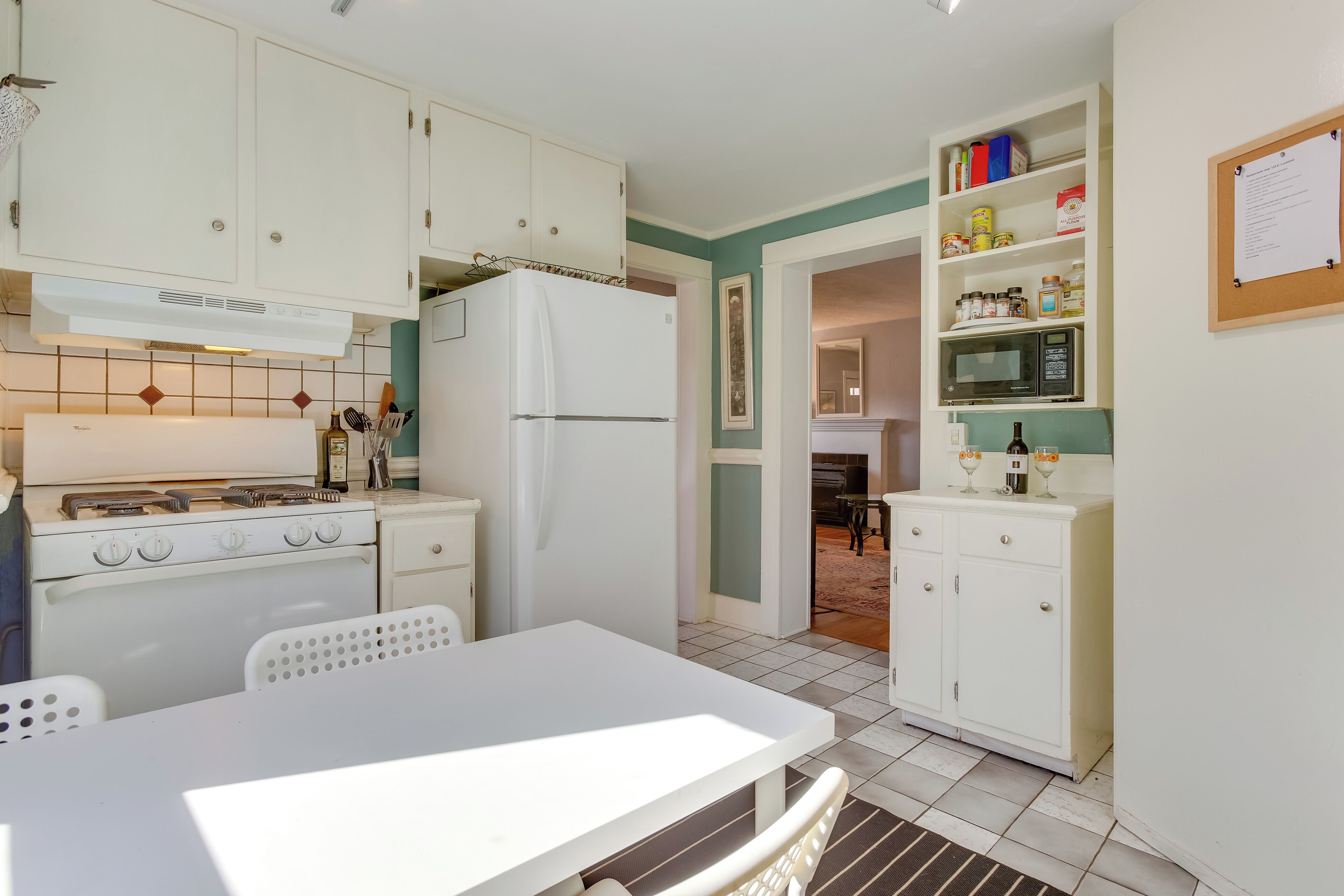A compact kitchen with white cabinets, a stove, a refrigerator, and a dining area with a table and chairs.