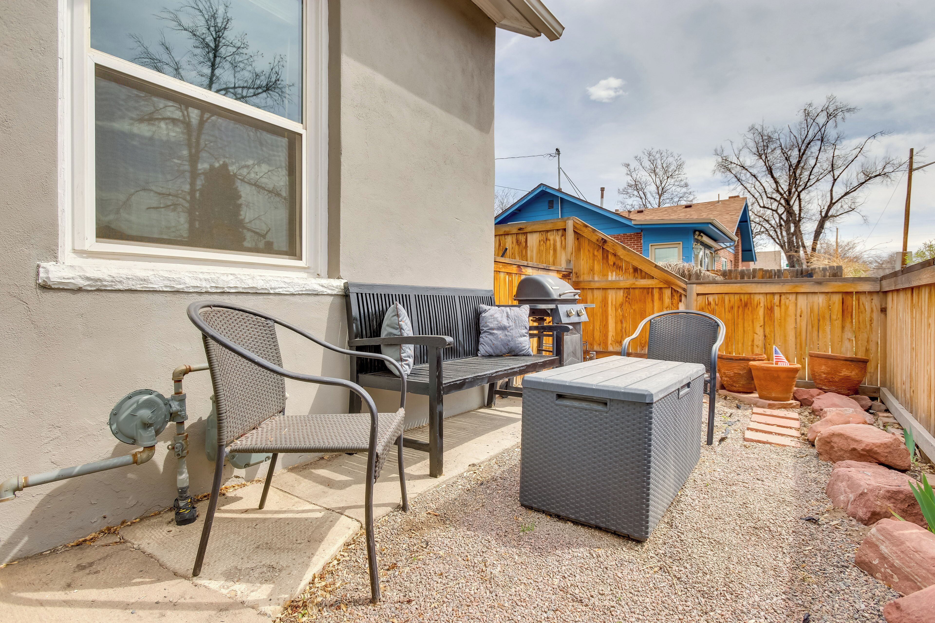 Une terrasse extérieure avec un canapé gris, une table en osier et un barbecue.