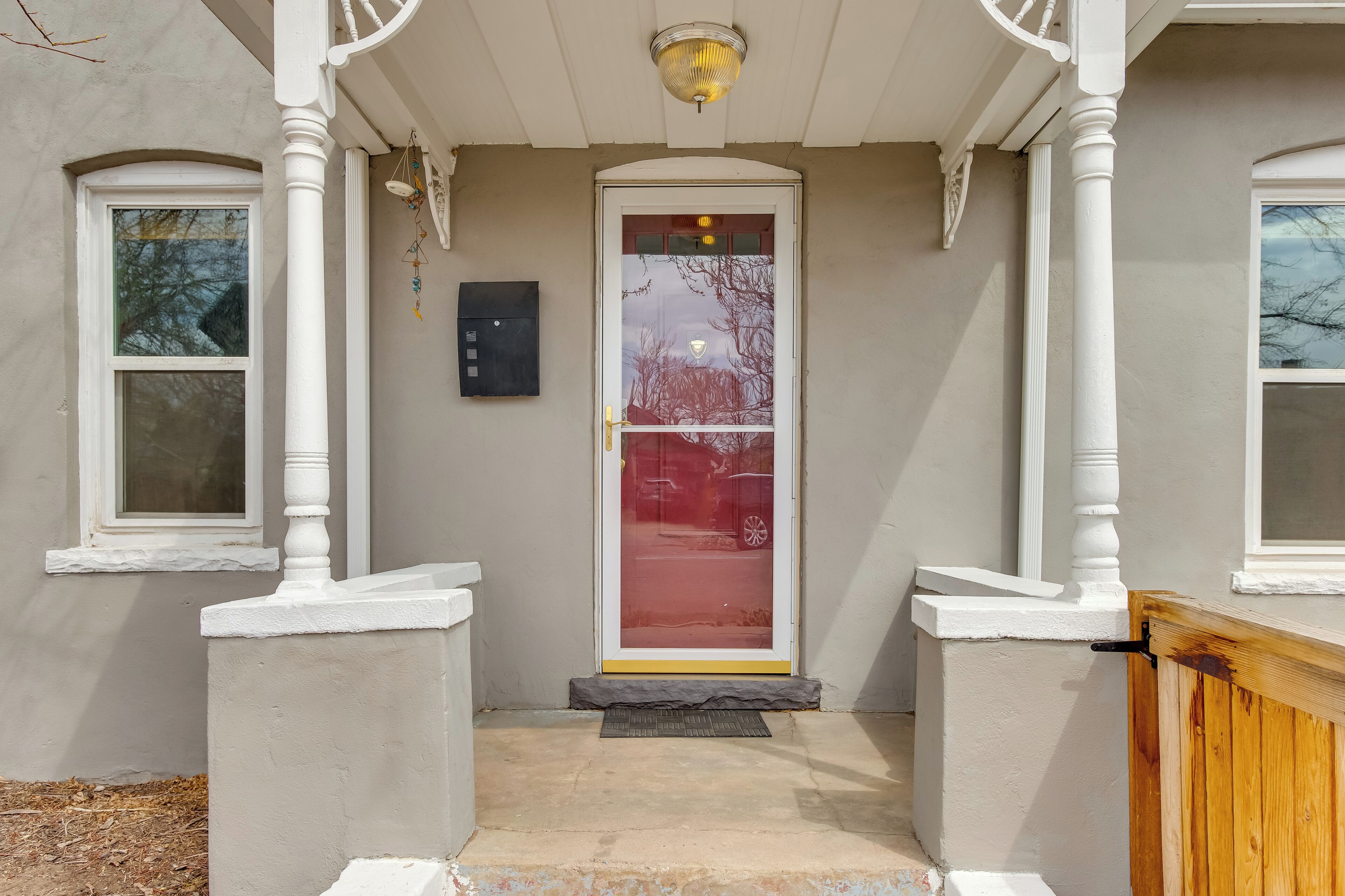 A house entrance with a white porch, a glass door with a red frame, and a mailbox on the wall.
