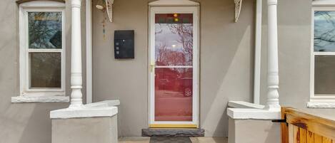 A house entrance with a white porch, a glass door with a red frame, and a mailbox on the wall.