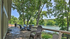 A wooden deck with outdoor furniture, overlooking a lake and surrounded by trees. - Lakefront Home w/ Fishing Dock & Fire Table! (Hollister)
