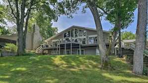 A two-story house with a balcony, surrounded by trees and a grassy yard. - Lakefront Home w/ Fishing Dock & Fire Table! (Hollister)