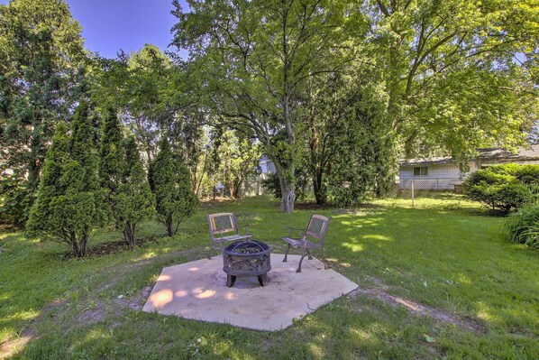 Un jardin avec un foyer, deux chaises et une pelouse.