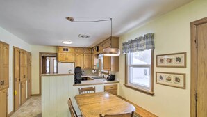 A kitchen with wooden cabinets, a central island, a dining table with chairs, a built-in bench, and a hanging pendant light. - Cozy Oshkosh Home, 4 Blocks to Lake Winnebago (Oshkosh)