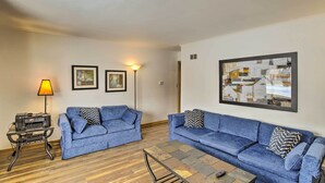 A living room with two blue sofas, a coffee table, a lamp, and framed artwork on the walls. - Cozy Oshkosh Home, 4 Blocks to Lake Winnebago (Oshkosh)