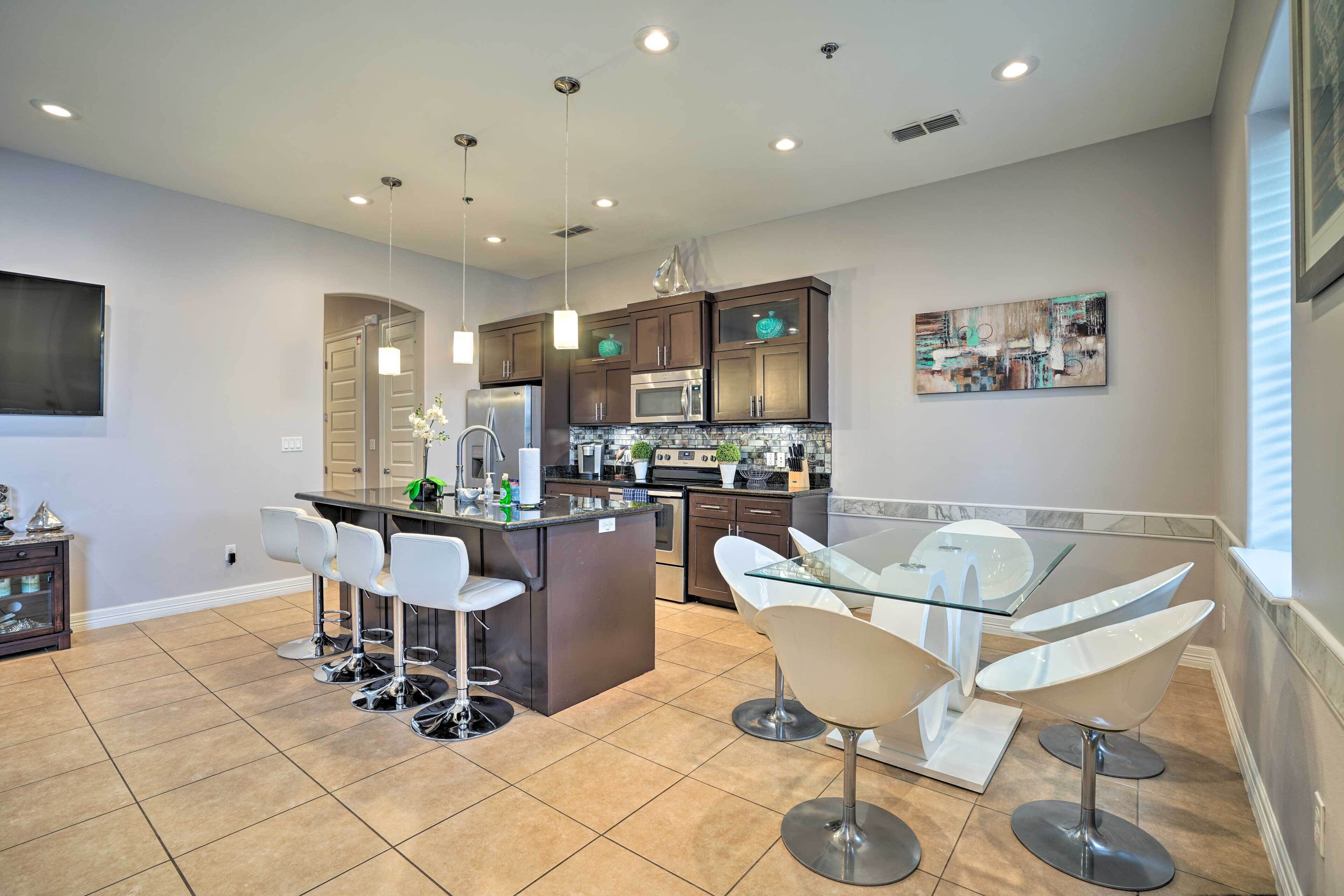 A modern kitchen with a central island, bar stools, a glass dining table, and contemporary appliances.
